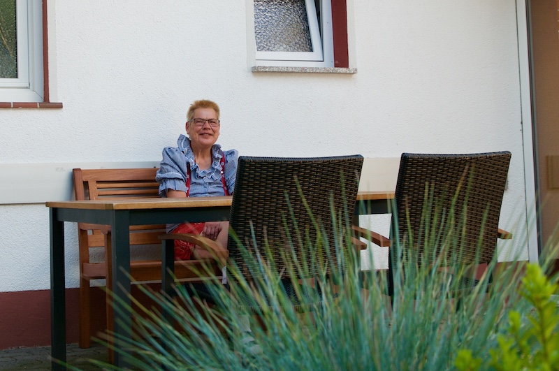 Bewohnerin auf einer Gartenbank vor dem Haus